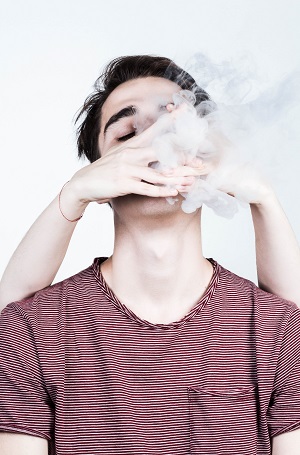 "young male with hand over his mouth and vapor coming out"