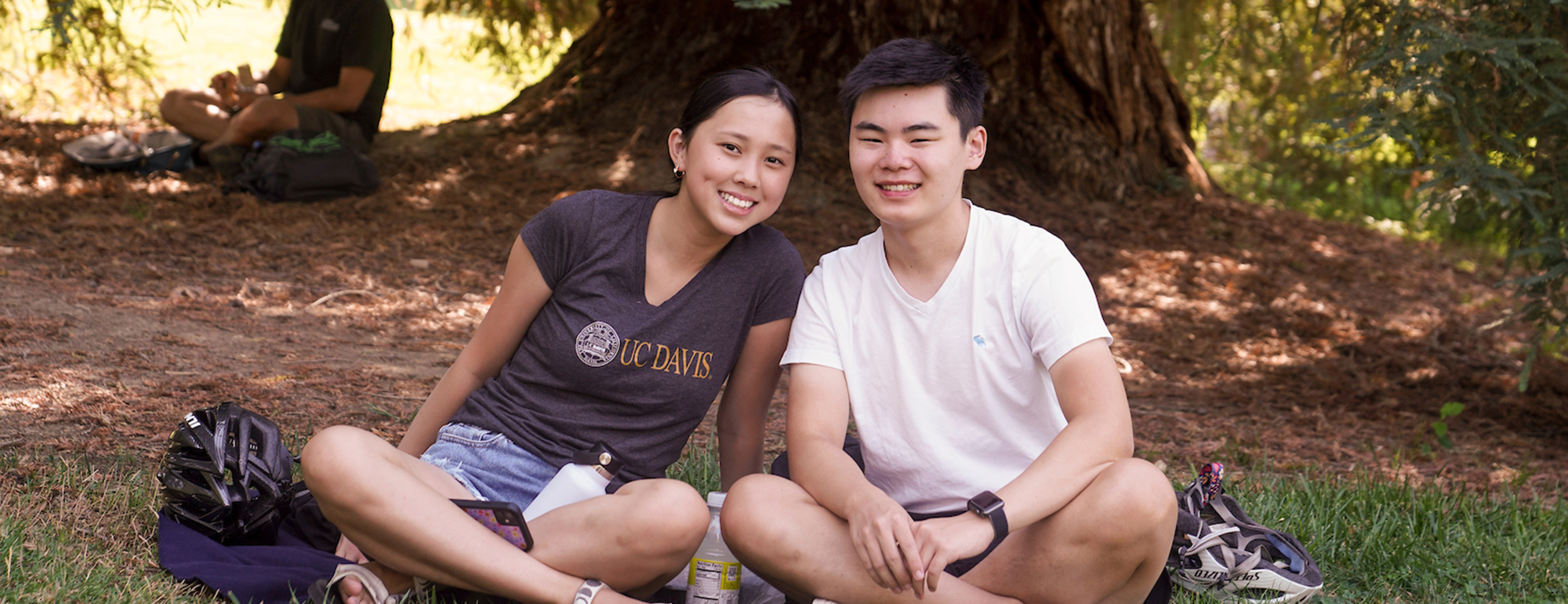 Image of two students sitting cross-legged in front of a redwood tree.