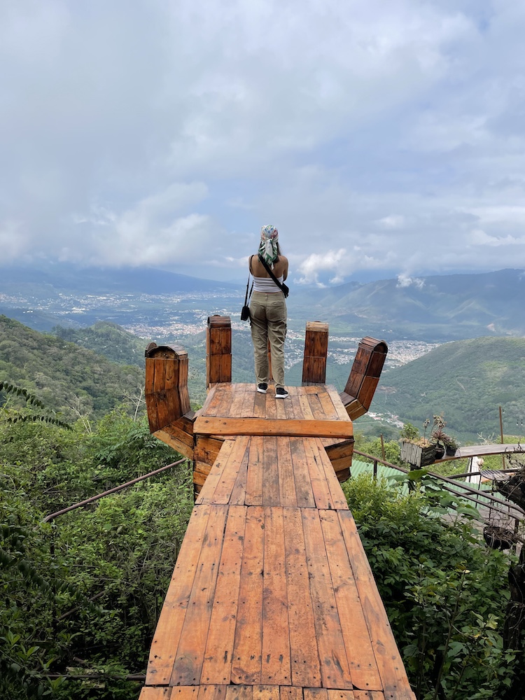 Someone standing on a large wooden hand, high above green hills