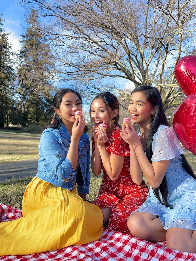 Three people pose with cupcakes outside on a picnic blanket