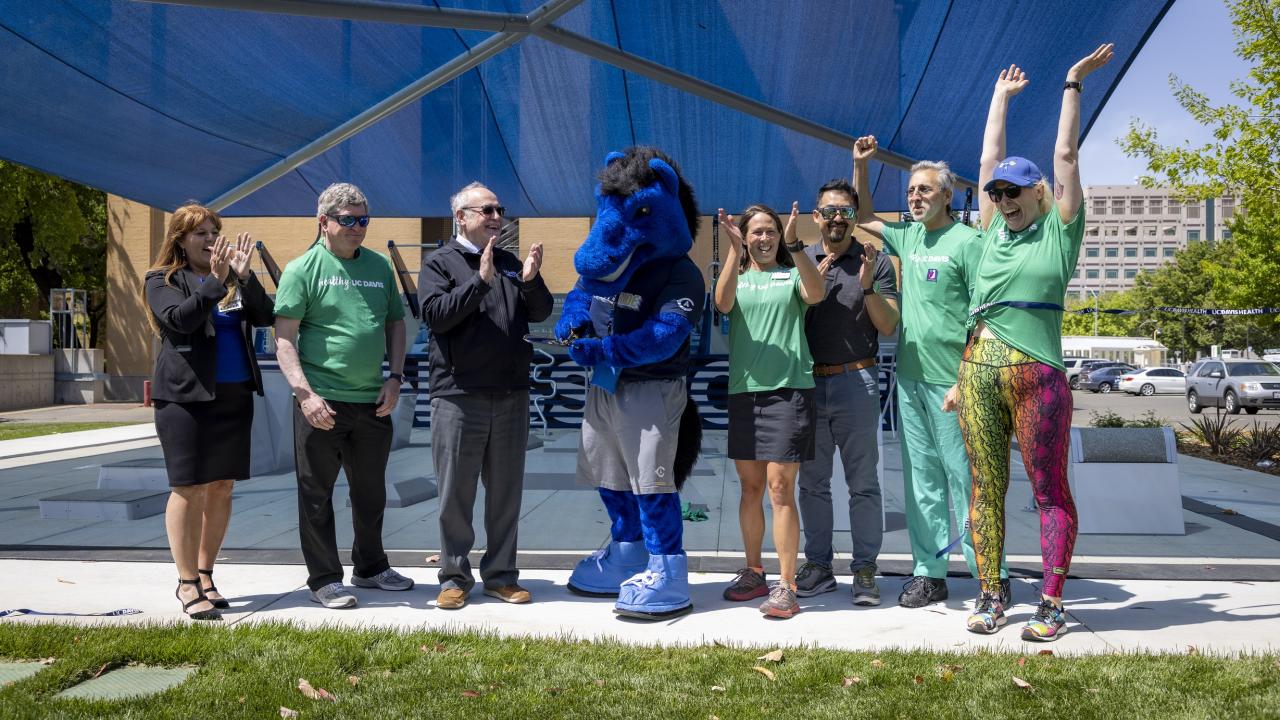 UC Davis Health leaders and staff surround Gunrock as he cuts the ribbon, signaling the opening of the outdoor fitness court