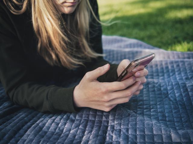 girl holding a phone laying on a blanket