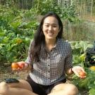 student sitting in a garden patch holding tomatoes