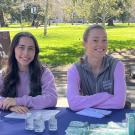 two students sitting at a table with a tablecloth saying "aggie mental health"